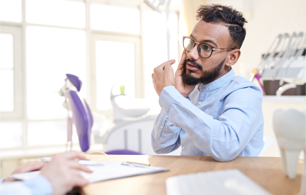 A patient sits across the desk from his dentist holding one cheek and describes their symptoms.