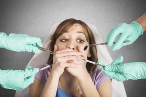 girl in dentist chair covering mouth because she is scared