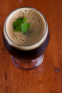Glass of dark beer with foam and a 4 leaf clover on top against dark oak wood background