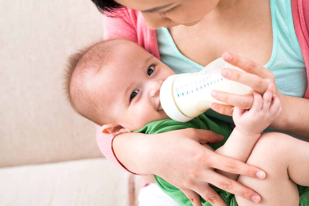 Mother holding smiling baby and feeding baby milk with bottle