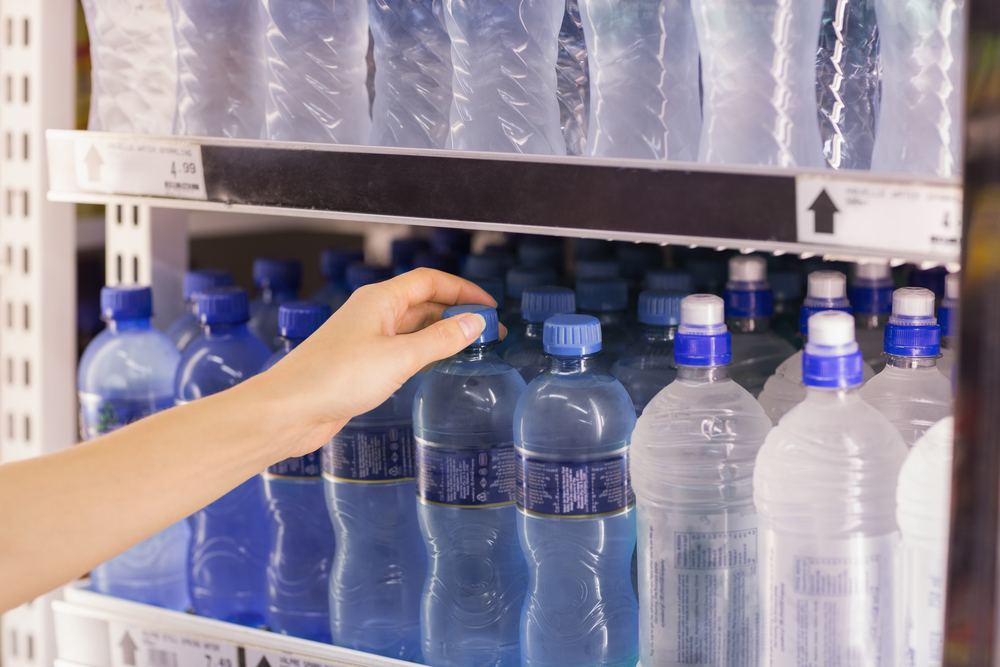 woman choosing blue bottle of water in store cooler among the bottled water options