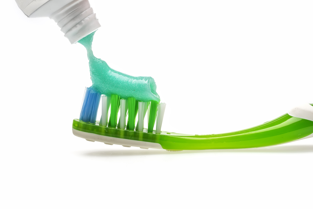 Soft green toothpaste being squeezed onto blue, white, and bright green bristles of bright green and white toothbrush
