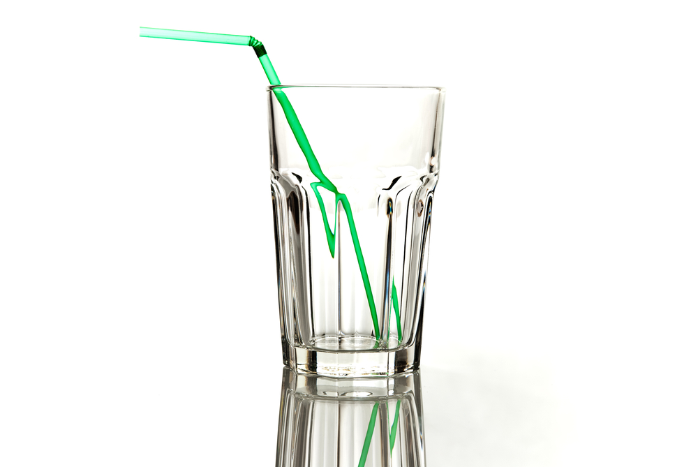 Clear, empty glass with green straw inside glass on white background