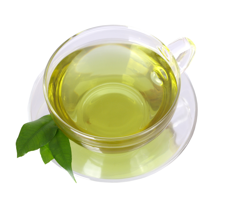 Cup of green tea in clear cup and saucer with green leaves sitting on edge of saucer on white background