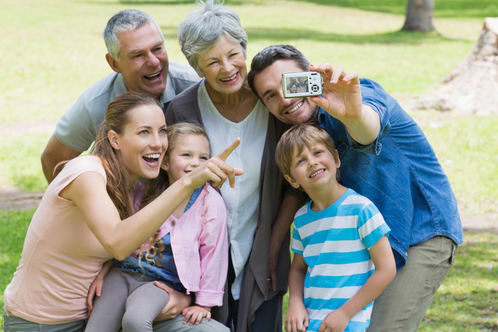 Man taking a picture with his wife, kids, and parents at a park on a sunny day