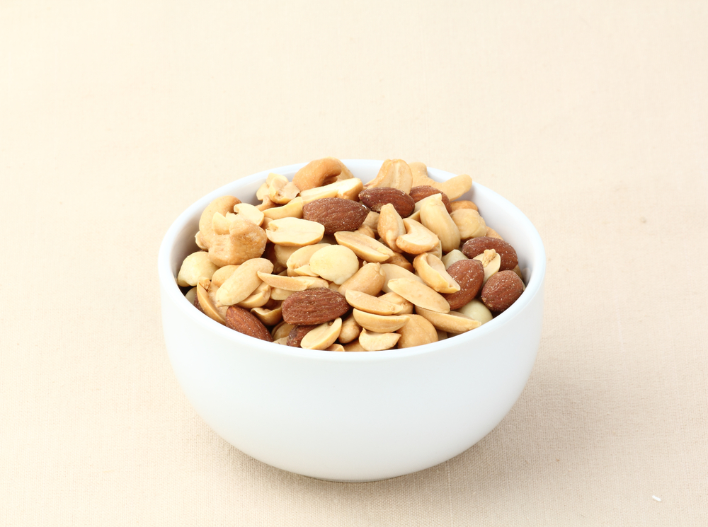 White cup of nuts (almonds, peanuts, macadamia) on light background