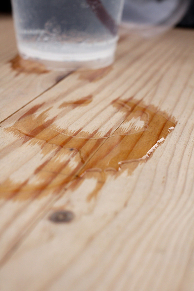 Water ring staining wooden table with glass of water sweating in background