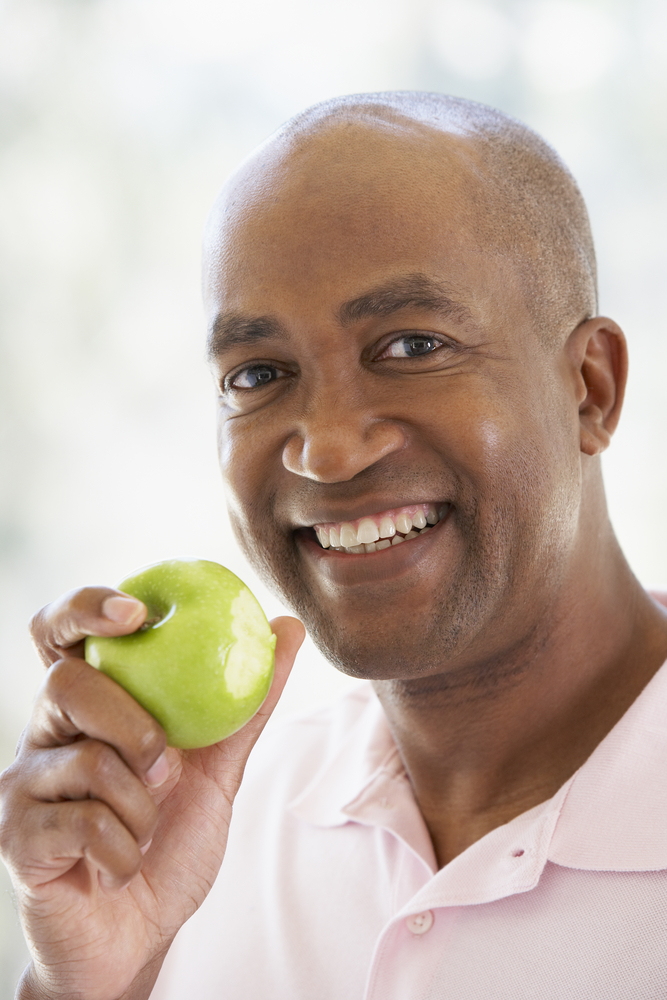 Man with beautiful teeth smiling at camera holding a green apple with a chunk already eaten