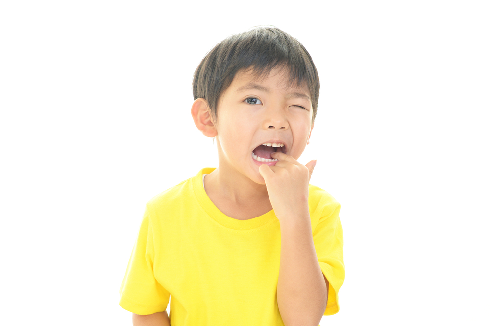 Little boy in yellow shirt pointing inside his mouth to a painful tooth that has a cavity