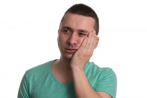 Man in green shirt with toothache holding side of face