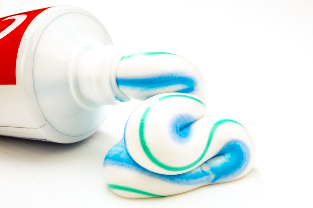 White, blue, and green stripe toothpaste oozing out of Colgate tube