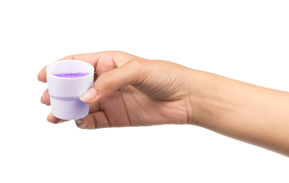 Woman's hand holding cup of purple mouthwash