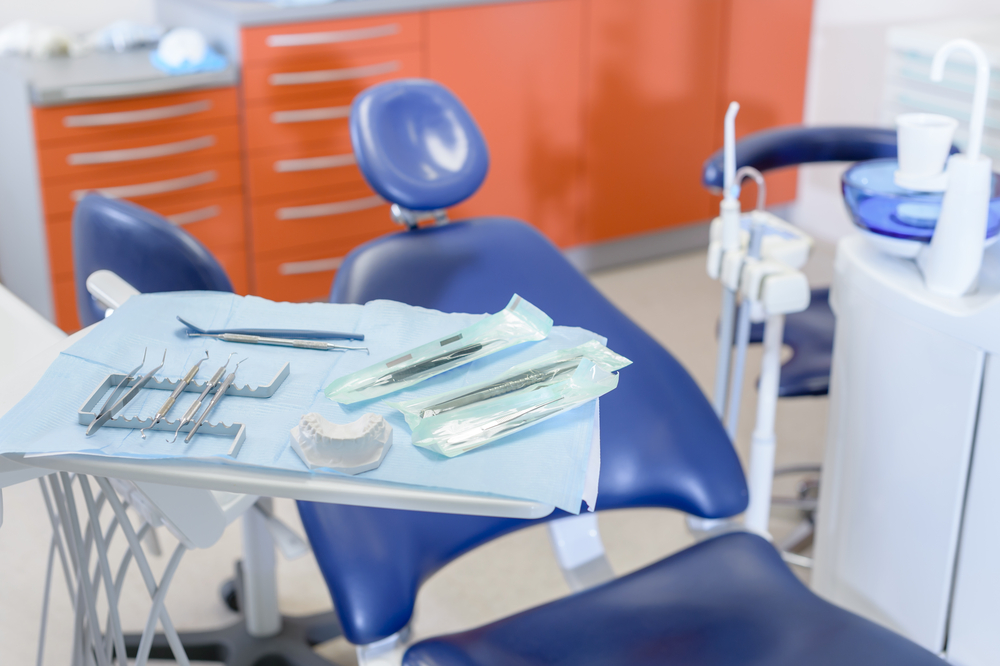 Dental chair next to tray with dental equipment and sink