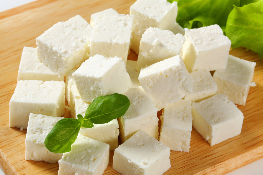 Group of feta cheese cubes with garnish on wood cutting board with lettuce in background