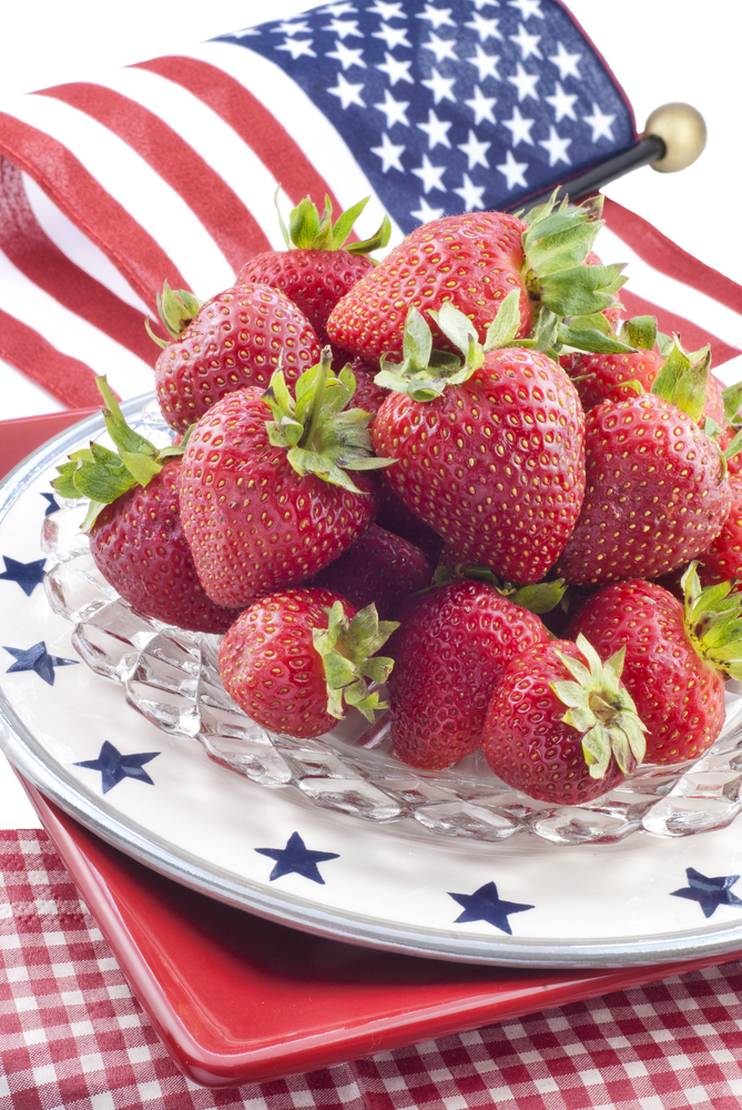 Bowl of strawberries on glass dish with blue stars and American flag in background