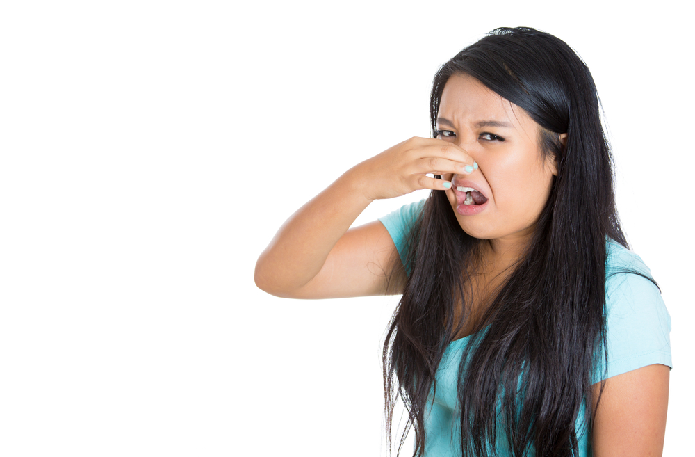 Woman in blue shirt holding nose because of her bad breath