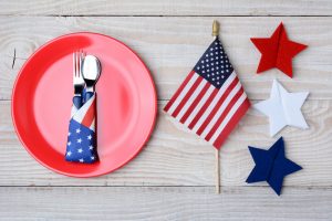Patriotic table set up red plate with silverware wrapped in red white and blue napkin American flag and red white and blue starts on wooden table
