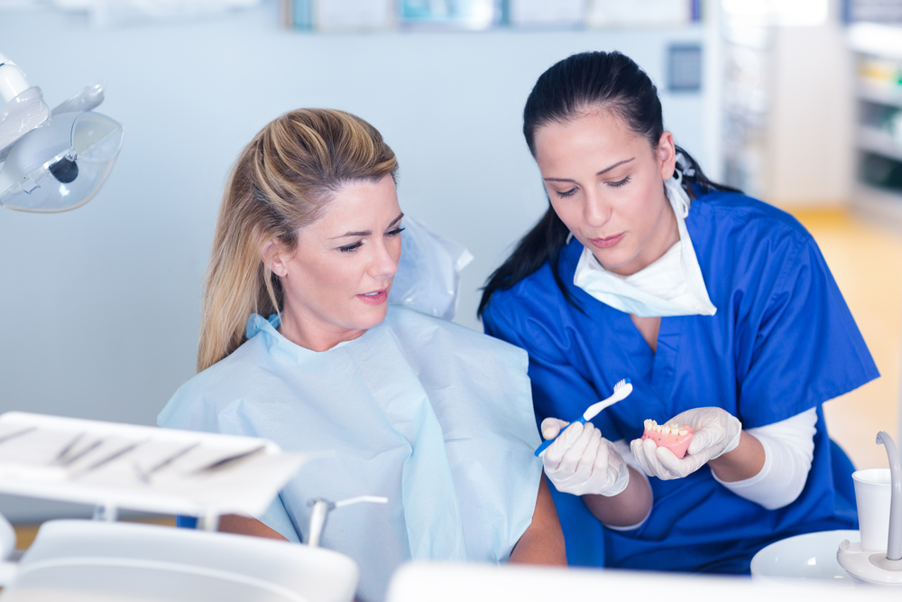 Dental hygienest woman showing woman patient how to properly brush teeth
