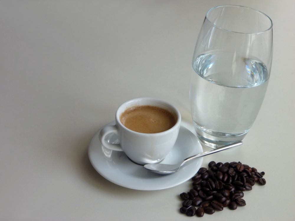 Cup of coffee on saucer with spoon next to coffee beans and glass of water