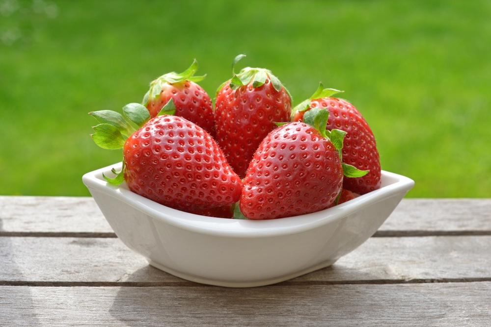 Bowl of strawberries on picnic table with green grass in background