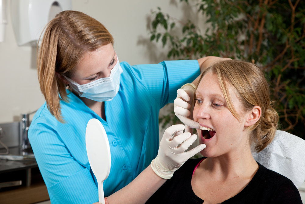 Woman patient watching with mirror dental hygienest woman show her how to properly floss her teeth