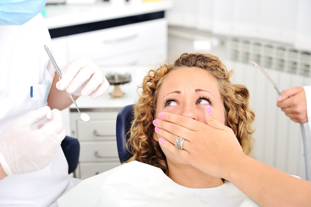 Woman in dental chair covering mouth because of dental anxiety dental fear dental phobia preventing dentist and dental hygienist from examining her mouth