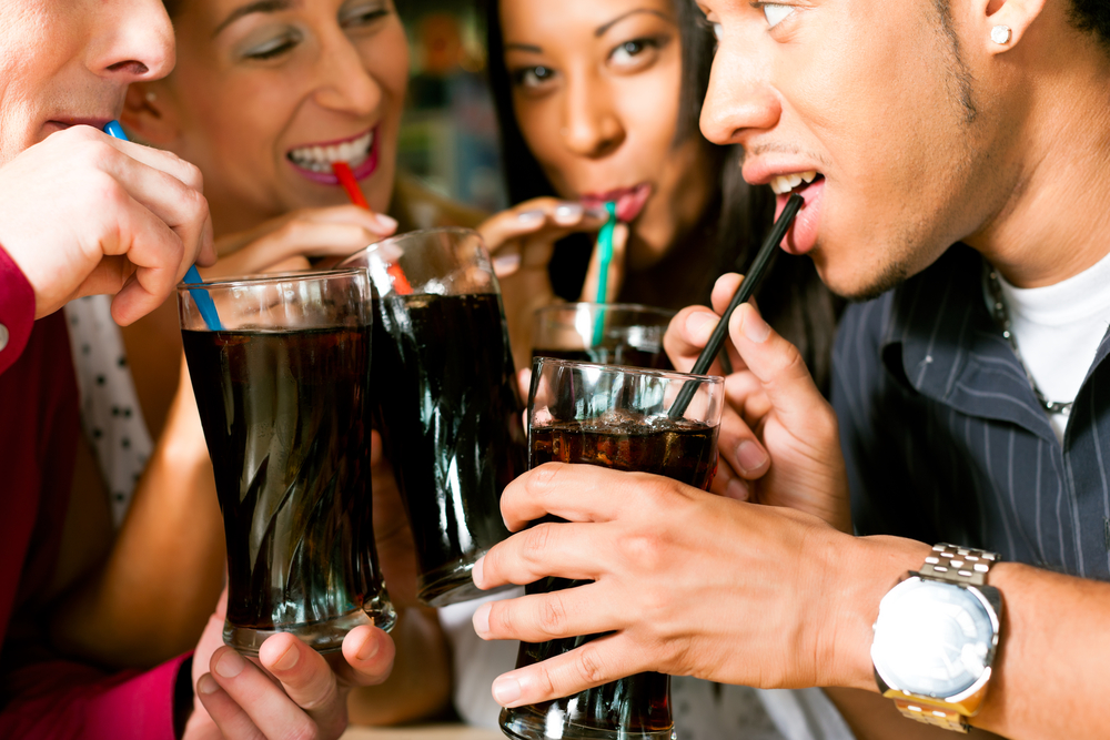 Group of 4 friends drinking glasses of soda through straws