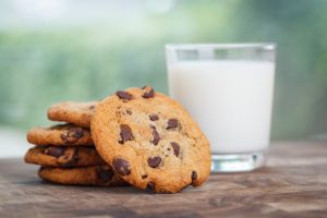 5 chocolate chip cookies stacked next to a glass of milk on a wood table