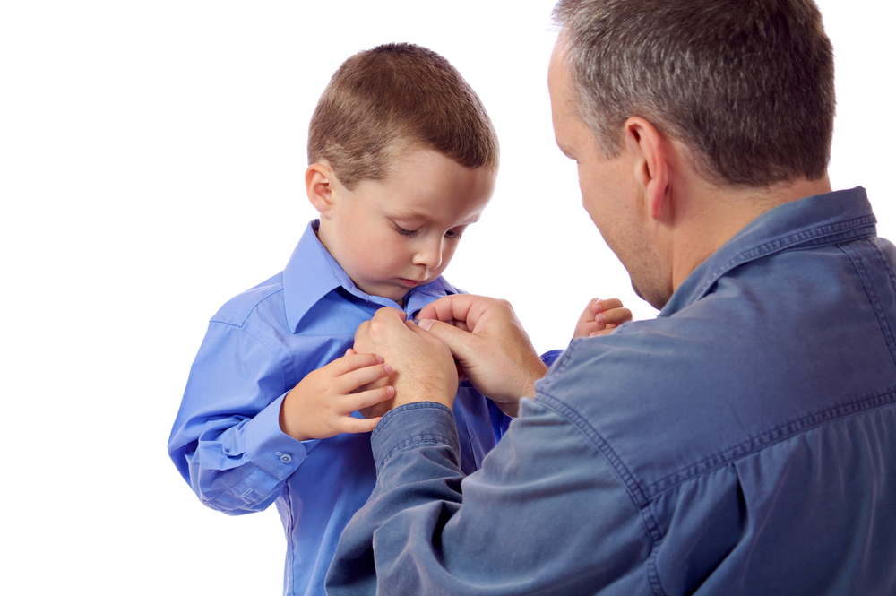 Father helping young toddler son button his shirt