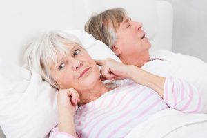 Wife holding ears in bed next to her husband who is snoring