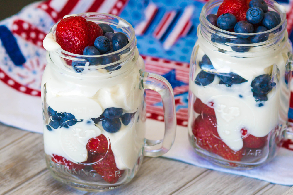 Greek yogurt with strawberries and blueberries in mason drinking jar with handle on picnic table with patriotic American 4th of July tablecloth