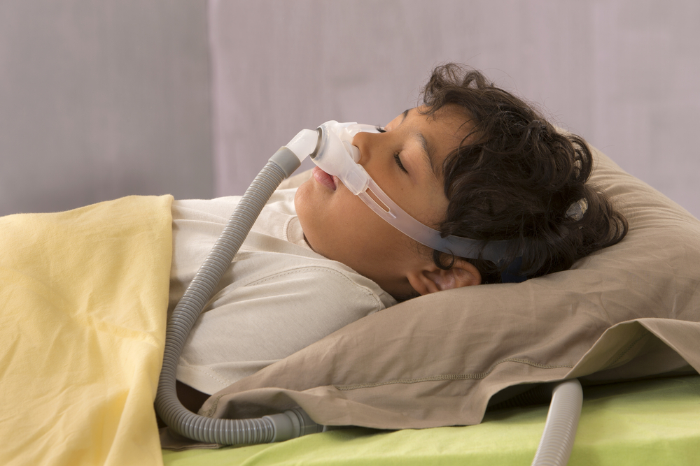 Little boy sleeping with a CPAP mask on his face to treat sleep apnea