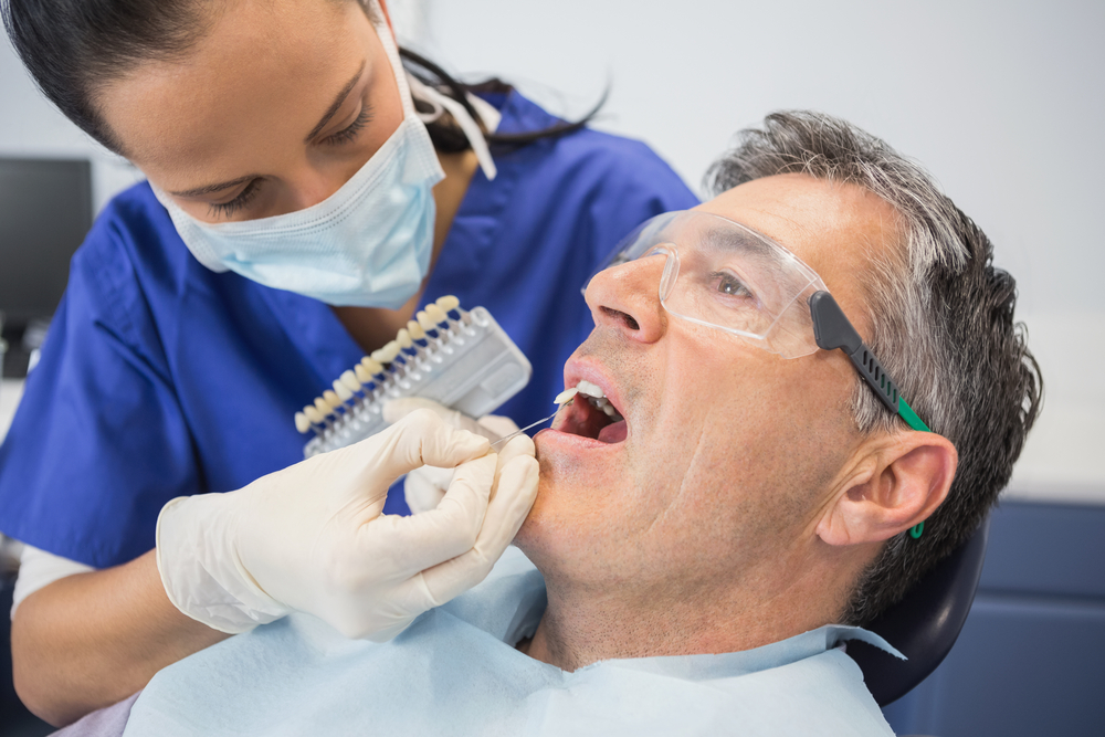 Dentist woman matching shade of patient's teeth for dental porcelain veneers