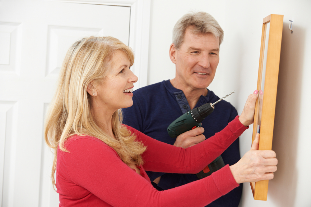 Husband with drill helping wife hang a picture on the wall