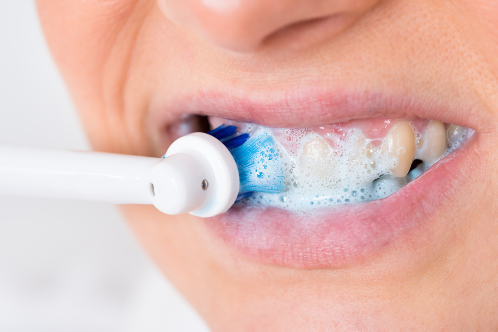 Close up of woman brushing her teeth with electric toothbrush and toothpaste