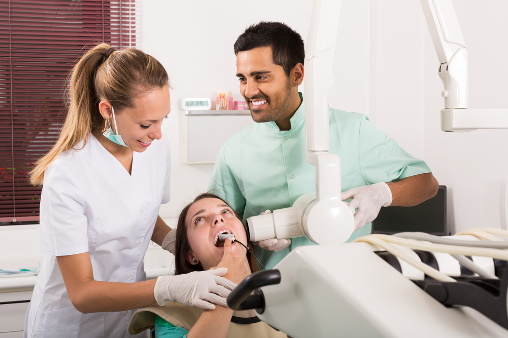 Dentist man helping dentist woman take a digital dental X-ray of woman's teeth