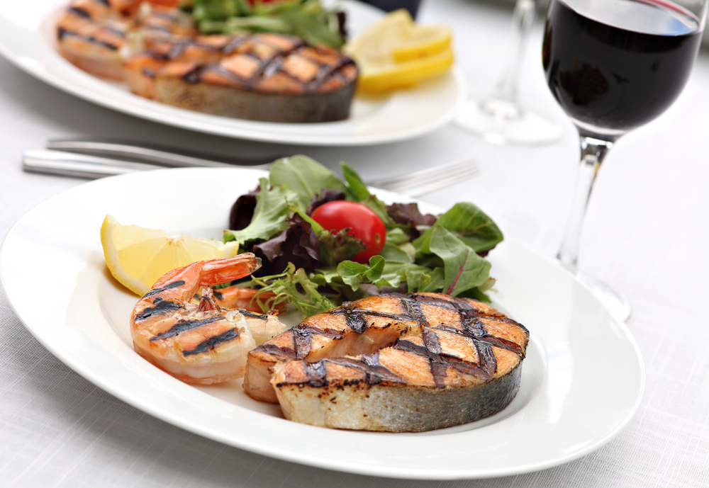 Grilled salmon with lemon and salad with tomatoes on plate with glass of wine