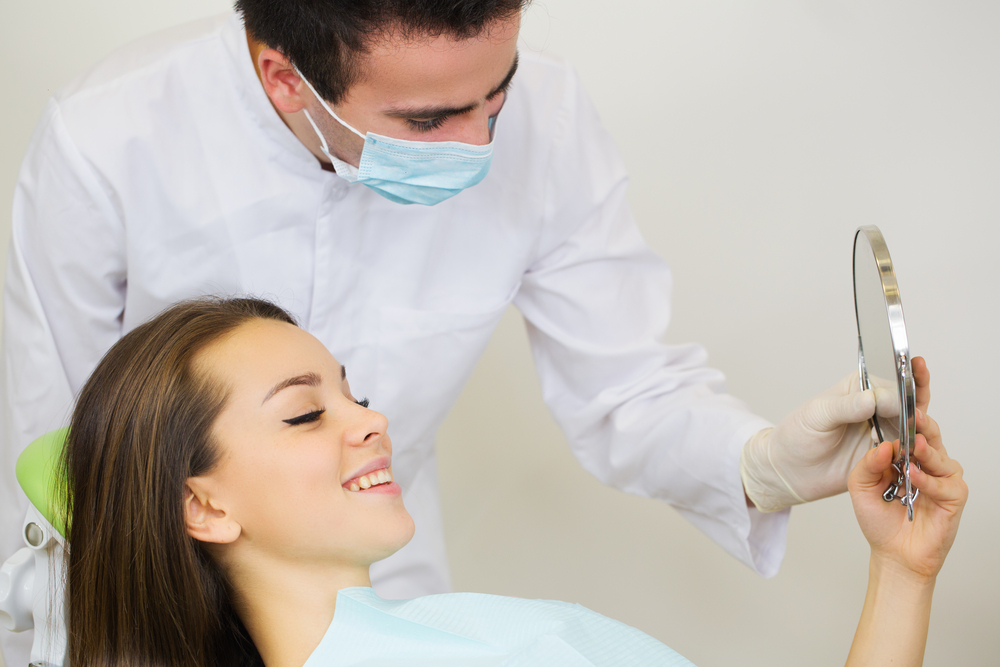 Smiling woman patient looking at teeth in mirror dentist man is holding