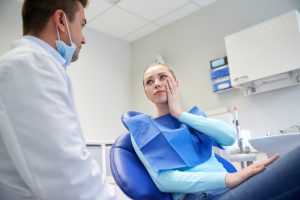 Woman patient in dental chair holding cheek toothache tooth decay talking to dentist man