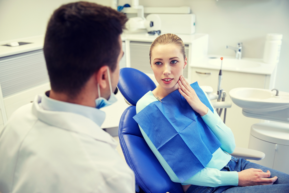 Woman patient in dental chair talking with dentist while holding the side of her face