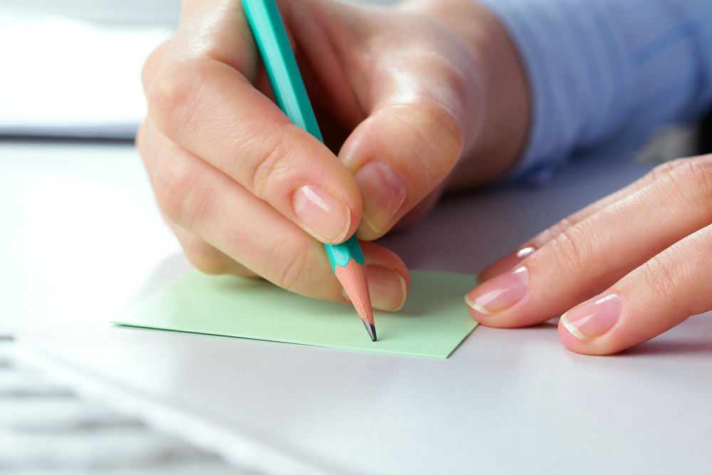 Close up of woman writing a note with a pencil on a post-it
