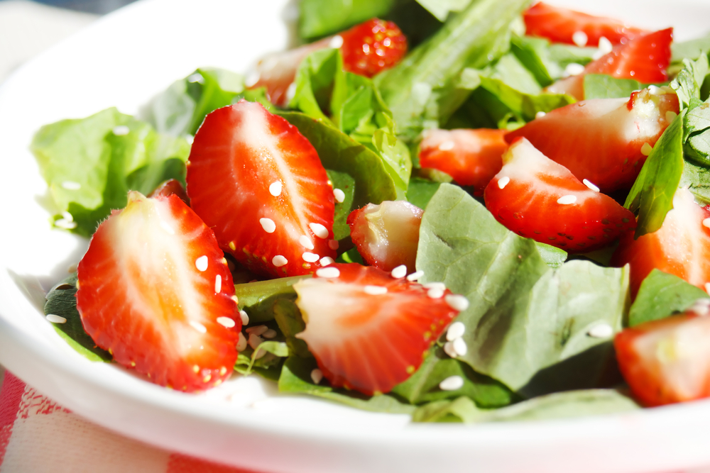 Strawberry salad with lettuce and seeds on white plate on red and white picnic tablecloth