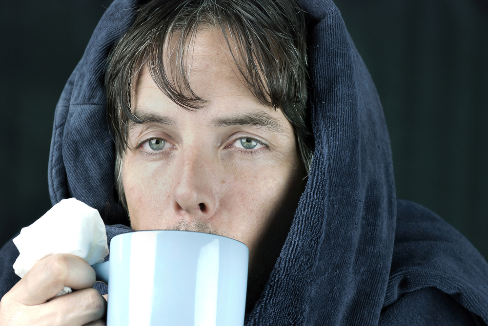 a man wearing a robe and holding a tissue is drinking ginger tea to mitigate his summertime sinuses