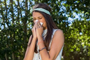 a girl surrounded by trees is sneezing due to summertime sinuses