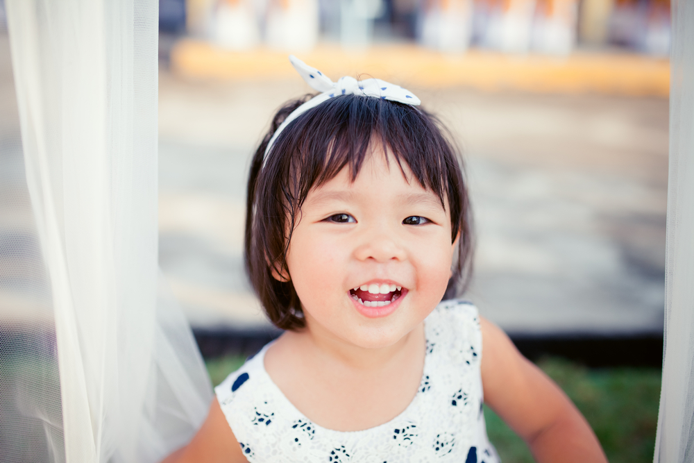 Little girl child showing front teeth with big smile: Healthy happy funny smiling face young adorable lovely female kid with new tooth dental loss: Joyful portrait of asian elementary school student