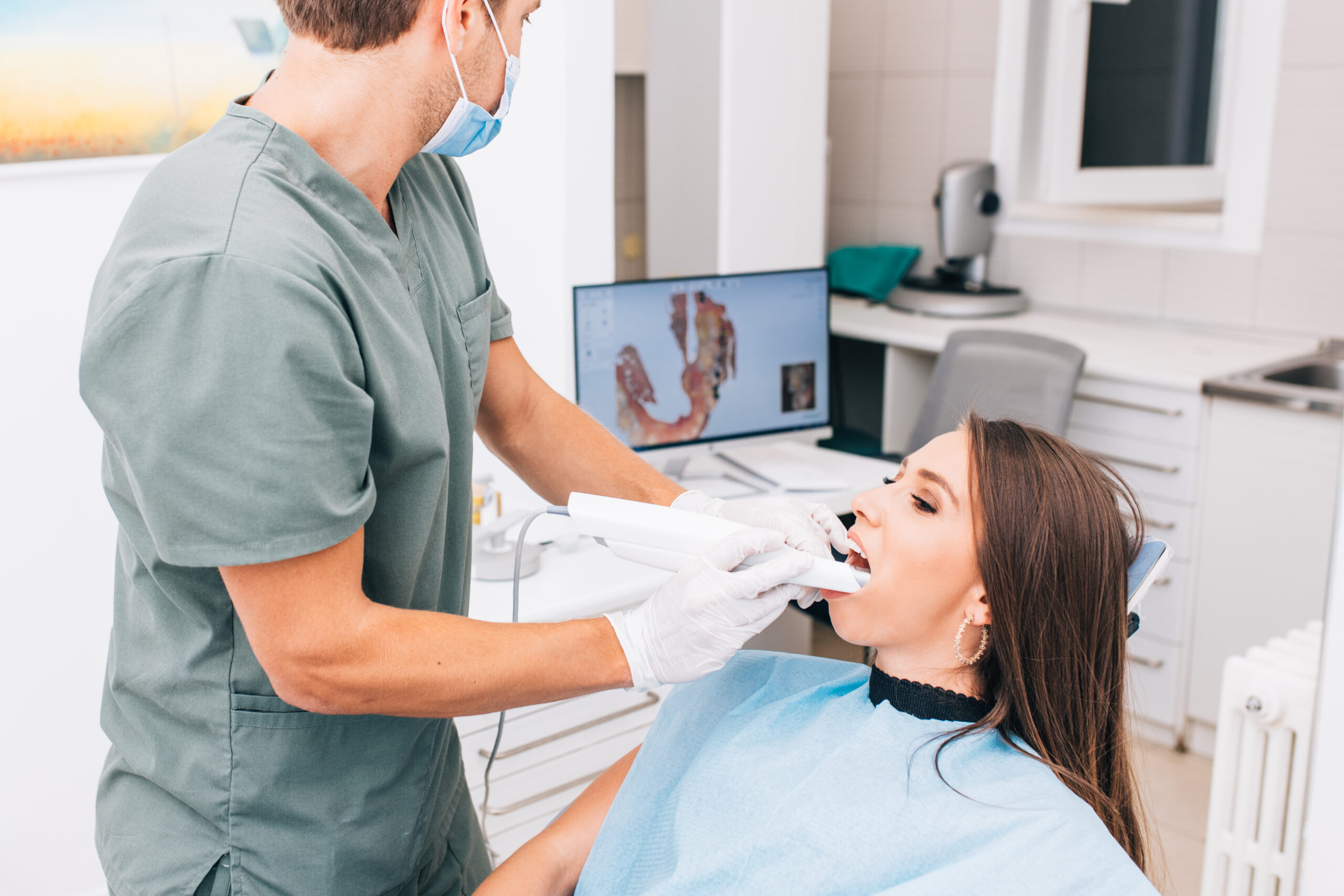 Стоматолог в маске и перчатках, используя СИЗ и универсальные меры предосторожности, проводит обычную чистку зубов в Хьюстоне, штат Техас.