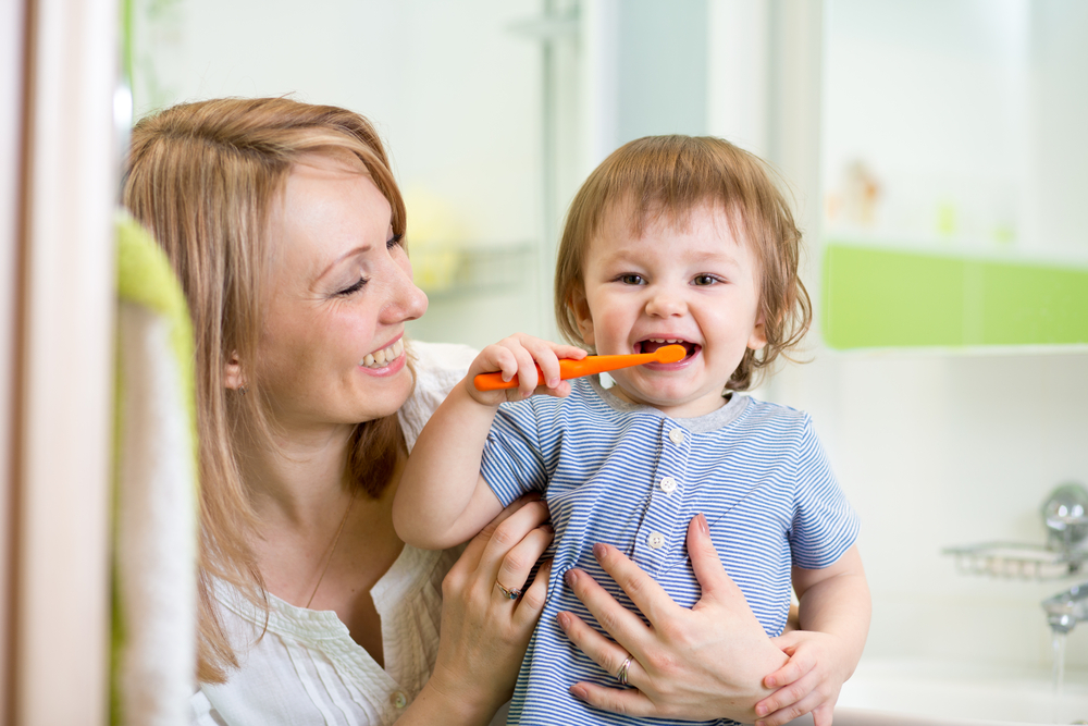 a mother watches and encourages her toddler to form good dental hygiene habits