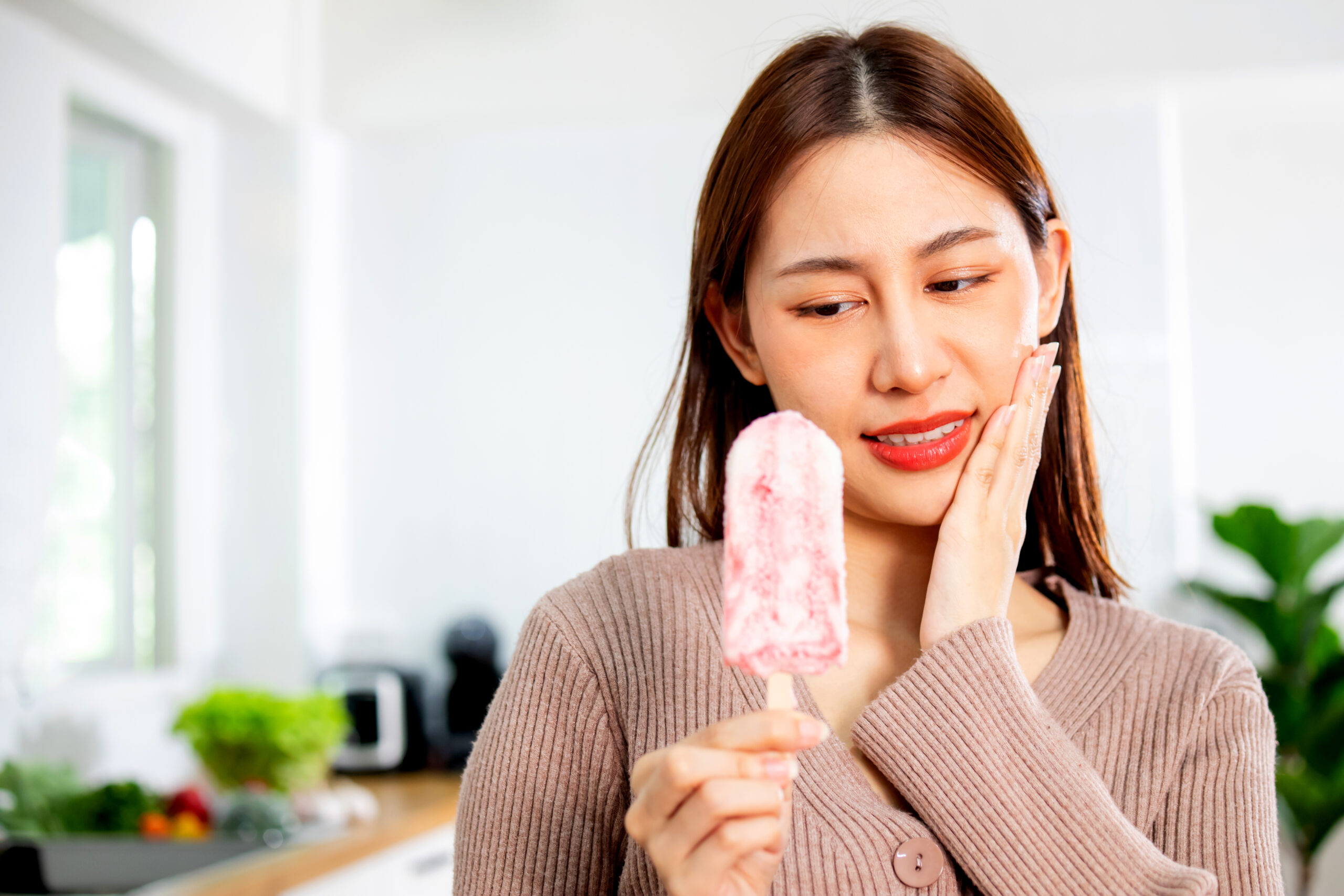 Asian woman has sensitive teeth while eating ice cream