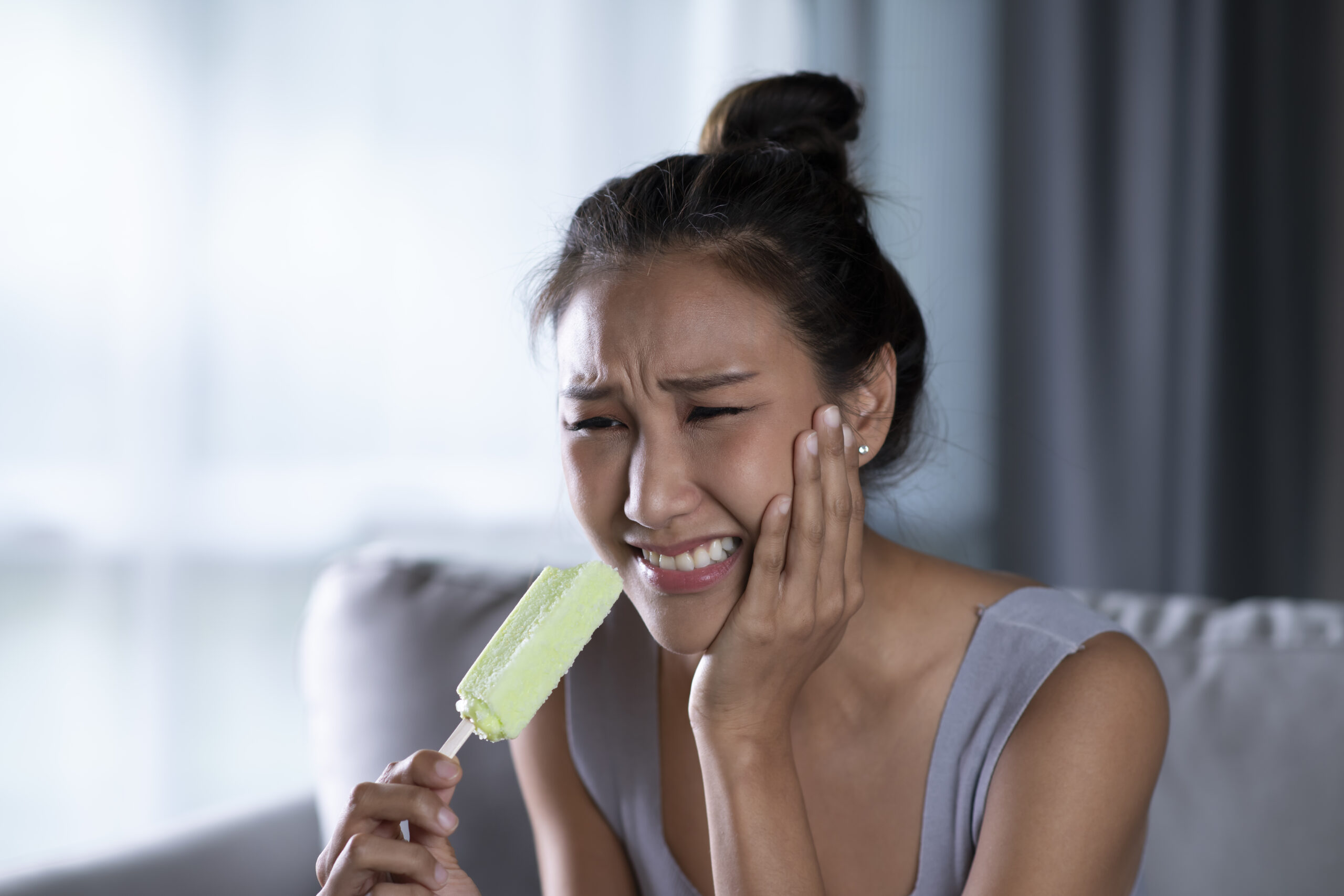 woman grabbing cheek in pain after biting popsicle