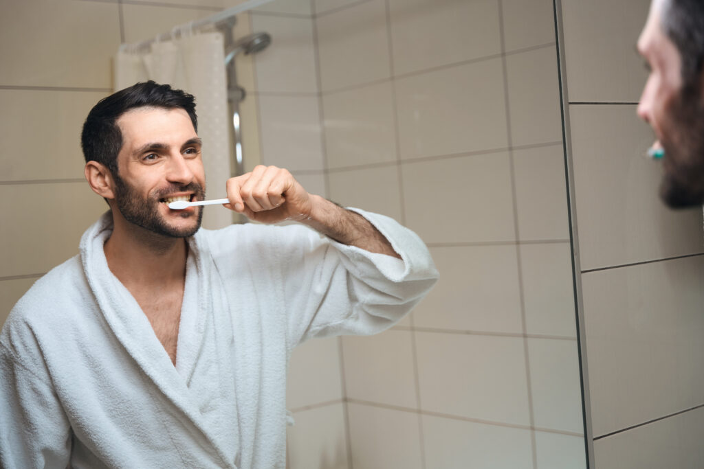 middle aged man brushing his teeth in the mirror